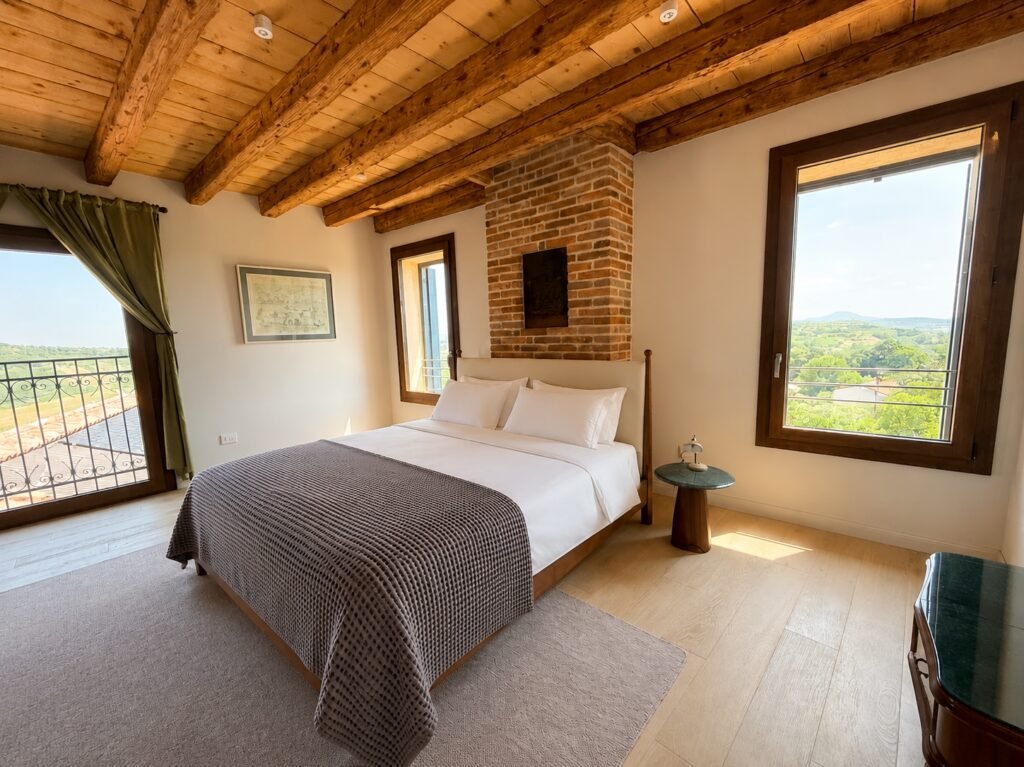 Suite Dogale bedroom with exposed brick, beamed ceiling and panoramic Colli Berici views